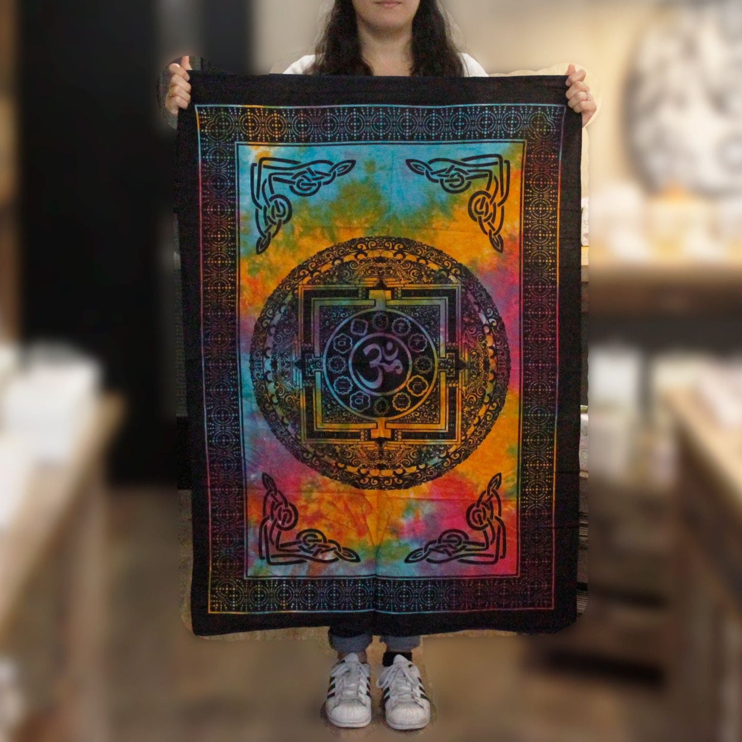 Alt Tag: Artisan Cotton Wall Art – Sacred OM 78x112 CM, multicolor algodón con símbolo OM central, persona sosteniendo tapiz vertical
