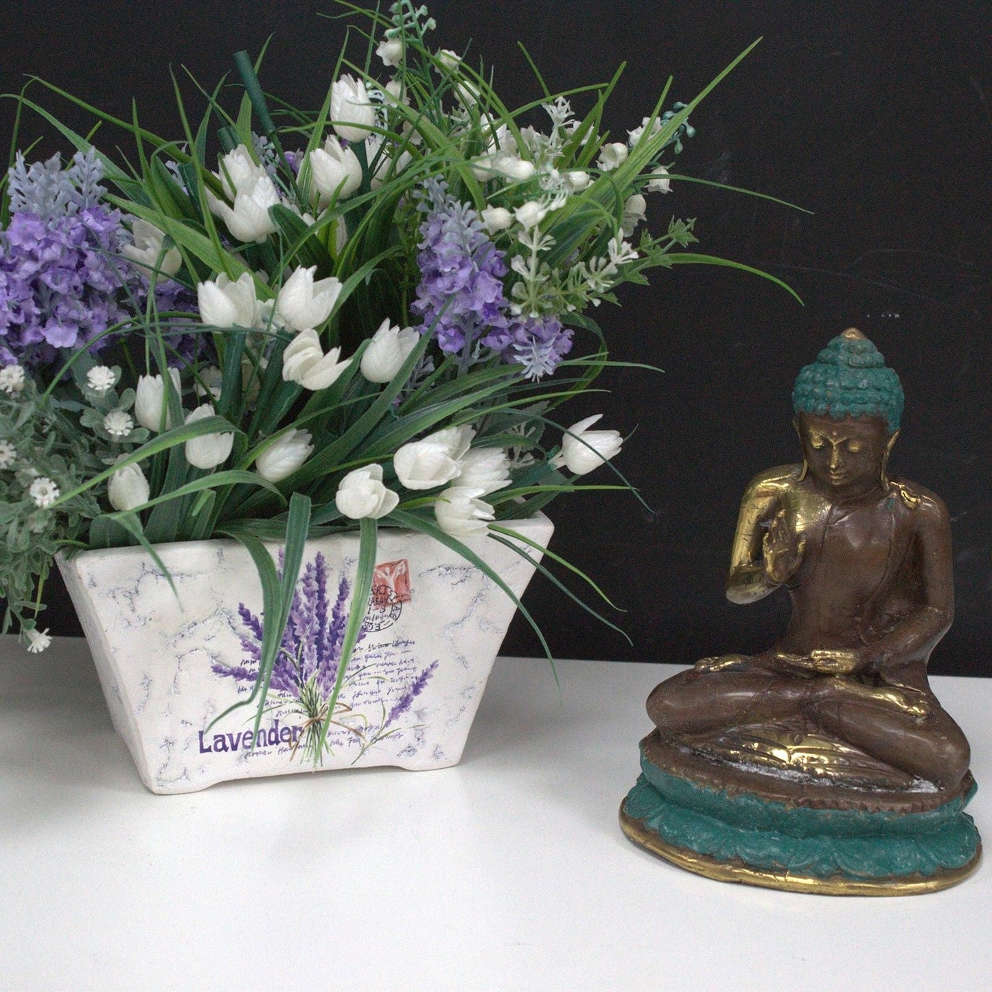 Alt Tag: Estatua de Buda de latón – Decoración Feng Shui de latón 10x5 CM en pose sentada junto a un arreglo de flores blancas y moradas