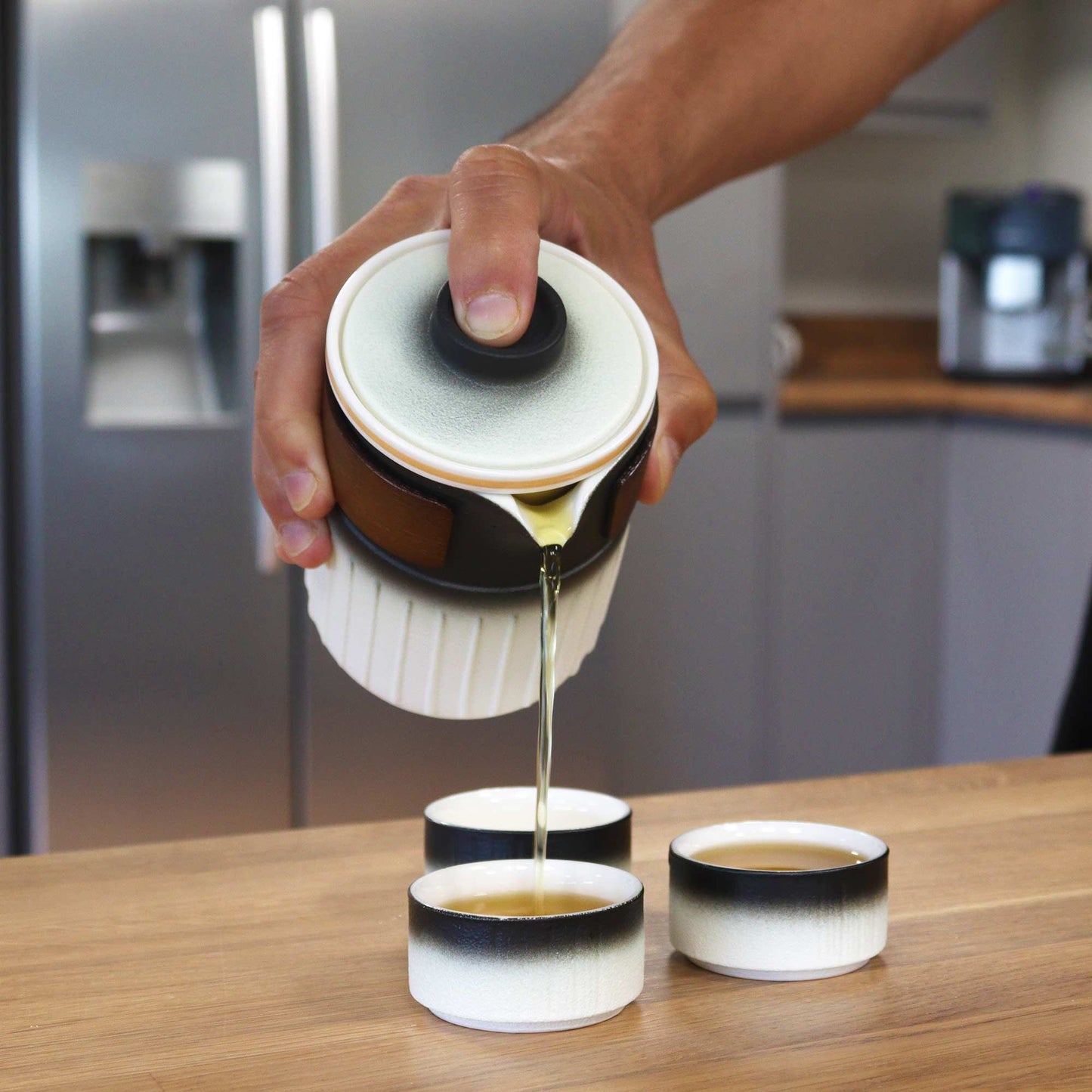 Ceramic Herbal Teapot Set – Travel Pack vertiendo té desde tetera de cerámica con degradado blanco a negro en tazas