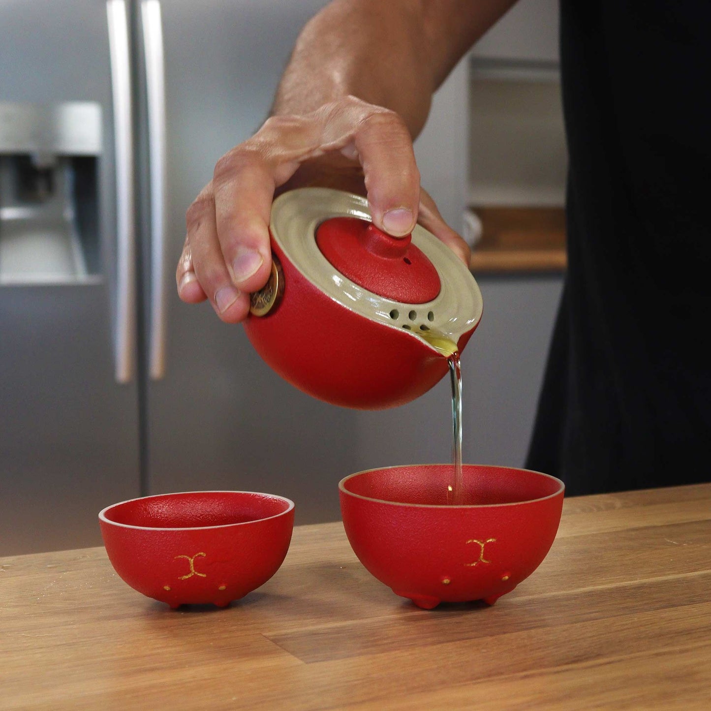 Money Cat Teapot Set – Two Cups – Travel Pack – Red ceramic teapot pouring tea into two red cups on wooden table