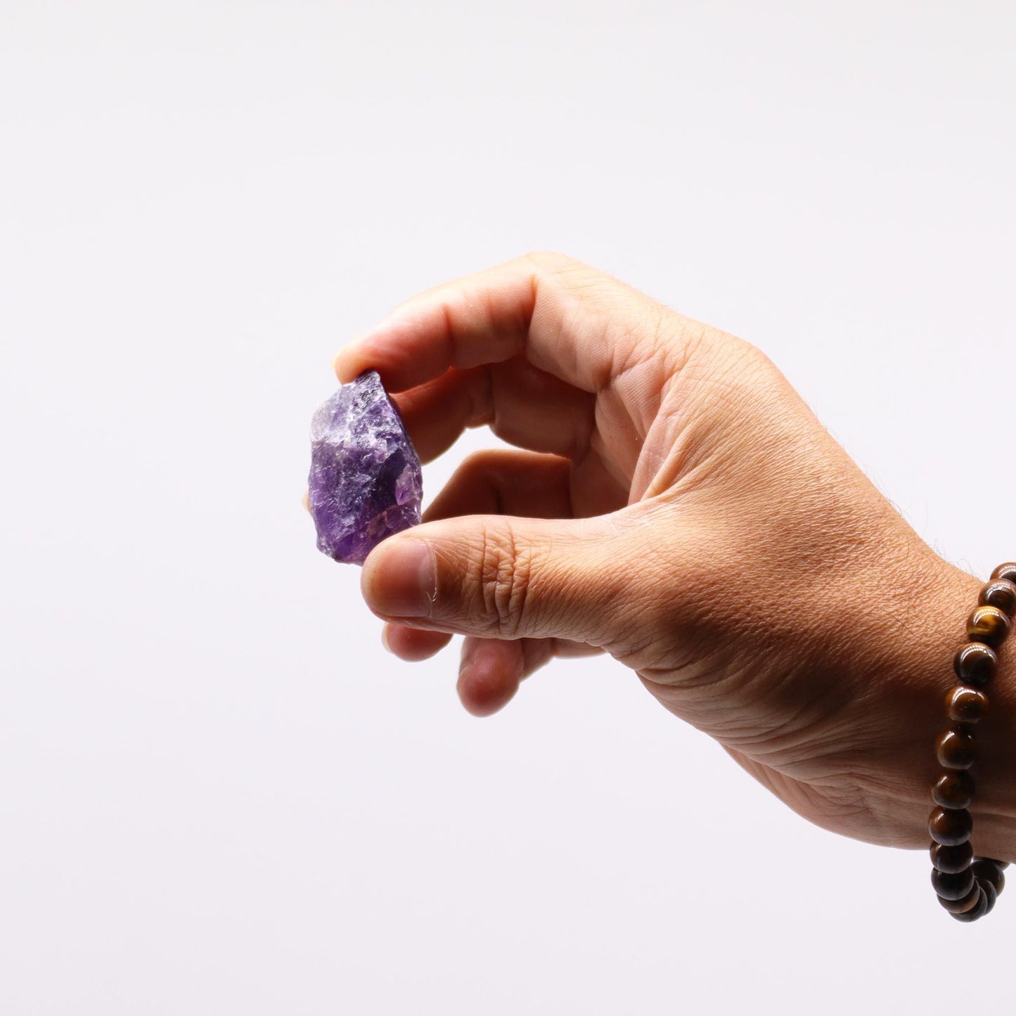 Alt Tag: Amethyst Gemstone – Raw Crystals 500GM, mano sosteniendo cristal de amatista en bruto morado sobre fondo blanco