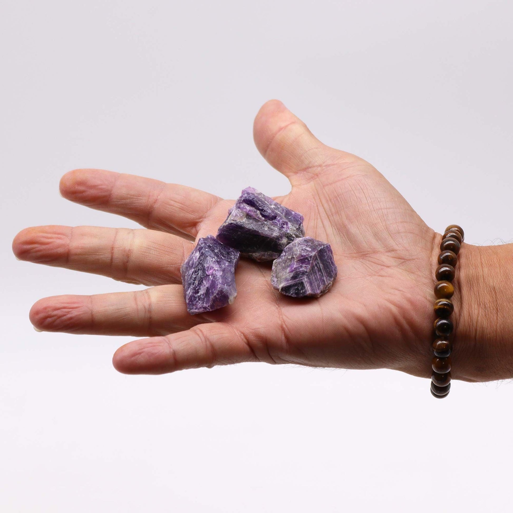 Alt Tag: Amethyst Gemstone – Raw Crystals 500GM, piedras de amatista en bruto color púrpura sobre la palma de una mano