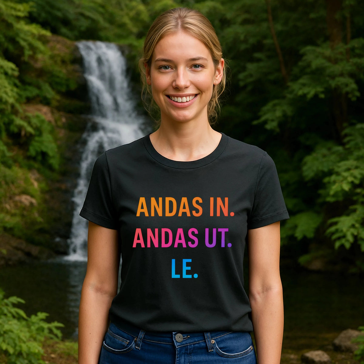 Alt Tag: Model wearing Andas Andas Ut Le Budskap 100% Organic Cotton T-Shirt with colorful text print, outdoors near waterfall
