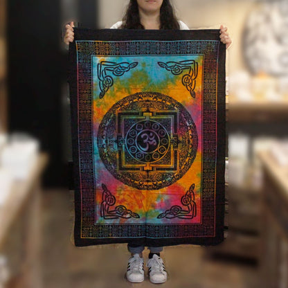 Alt Tag: Hantverksmässig väggkonst i bomull – Sacred OM 78x112 CM, flerfärgad bomull med centralt OM-symbol, person som håller i en vertikal tapetsering