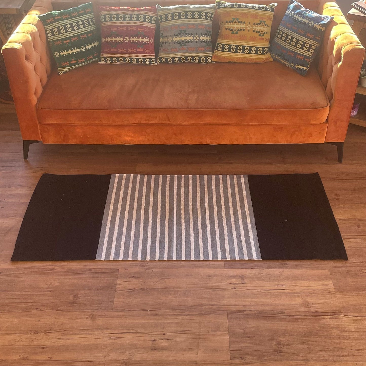 Handvävd bomullsmatta, hantverksmässig – 70x172 CM svart/grå på trägolv framför soffa, svarta kanter med grått randigt mittparti