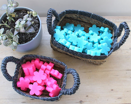 Cestas cuadradas de hoja de plátano – Set de 3 con asas sobre la mesa, con artículos coloridos en forma de flor junto a una pequeña planta en maceta