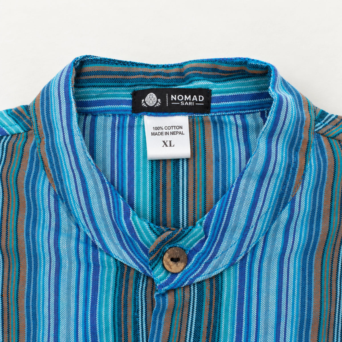 Close-up of the striped band collar with Nomad Sari branding and a label stating 100% cotton, made in Nepal and XL.
