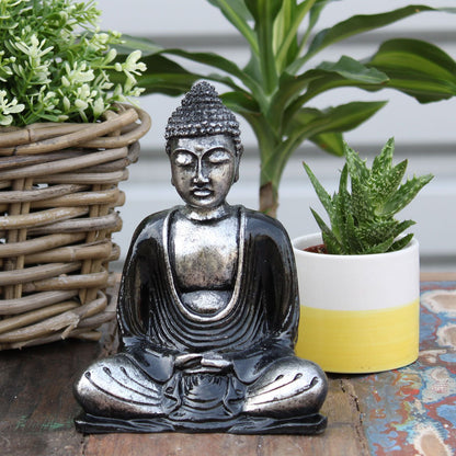 Alt Tag: Black & Grey Buddha Statue – Medium sitting statue with serene expression on rustic table beside potted plants