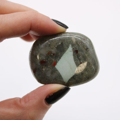 Gemstone Tumble Stones – Bloodstone Edition polished bloodstone tumble stone held between fingers, dark green with red flecks
