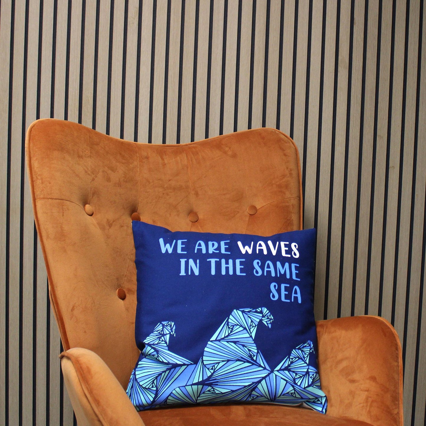 Alt Tag: Blått kuddfodral i bomull med dikt – 45x45 CM med citatet "We Are Waves" och vågillustration på en blå bomullskudde, på en orange stol
