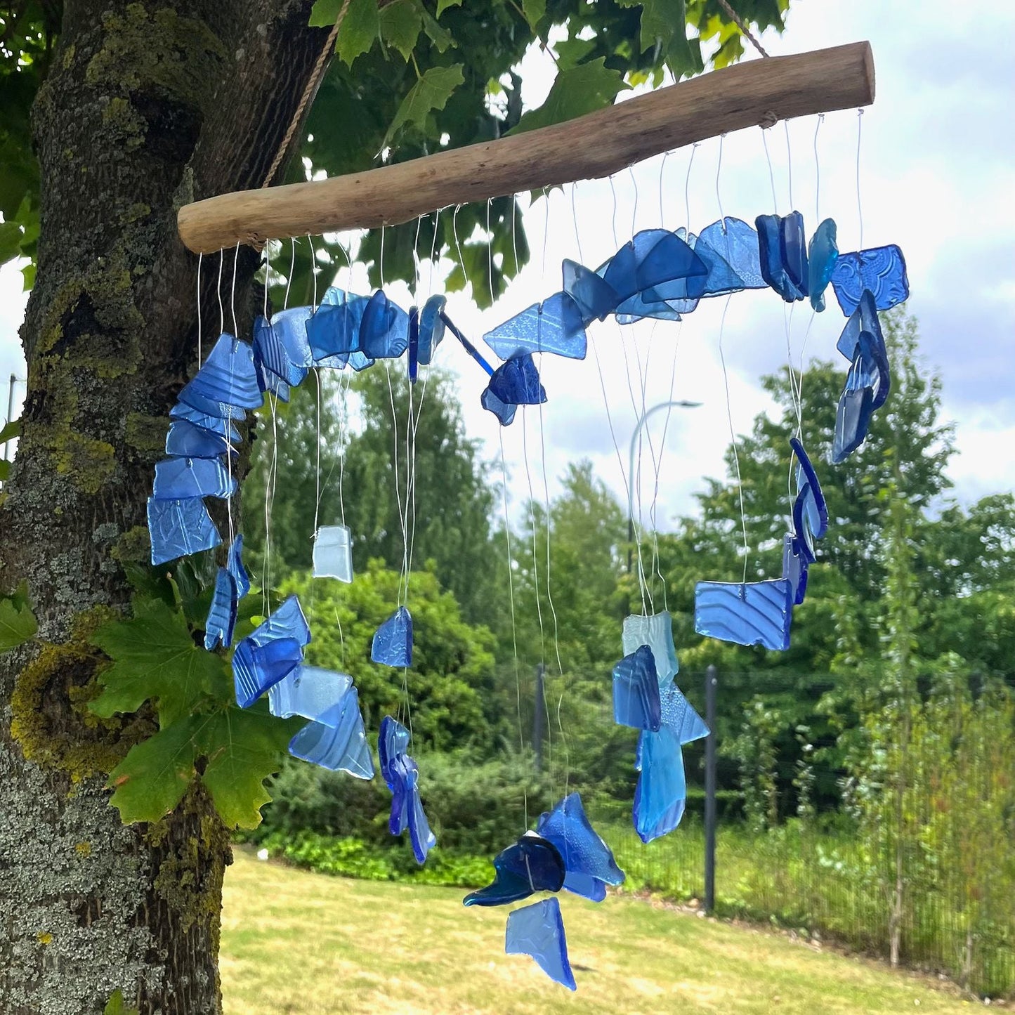 Alt Tag: Blå vindspel i återvunnet glas – 30x60 CM hängande från drivved med delar i återvunnet blått glas i trädgården