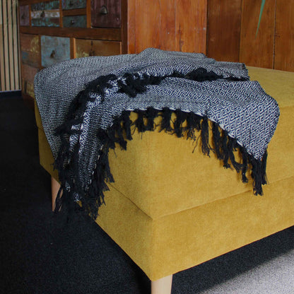 Boho Comfort Throw – kolgrå handvävd pläd i bomull med bohemisk textur och fransade kanter, draperad över en senapsgul ottoman