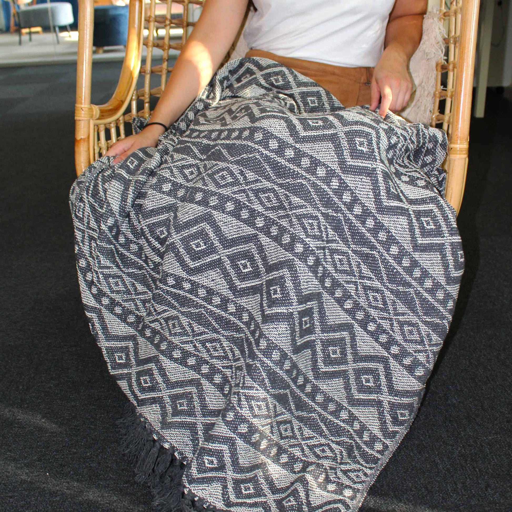 Alt Tag: Boho Comfort Throw – Grey Geometric grey geometric handwoven cotton throw blanket draped over seated person in rattan chair