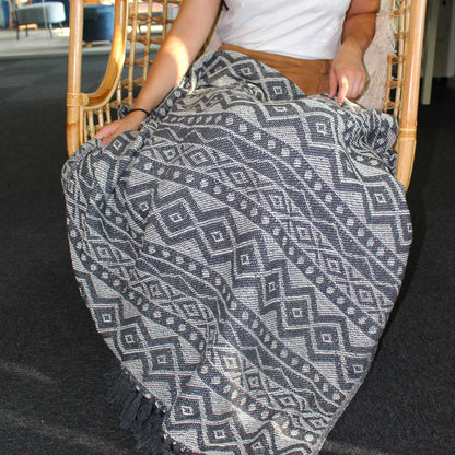 Alt Tag: Boho Comfort Throw – Grey Geometric grey geometric handwoven cotton throw blanket draped over seated person in rattan chair