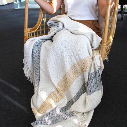 Alt Tag: Manta Boho Comfort – Manta de algodón tejida a mano Mellow Mattala con patrón de rayas en tonos tierra y bordes con flecos, colocada sobre una silla