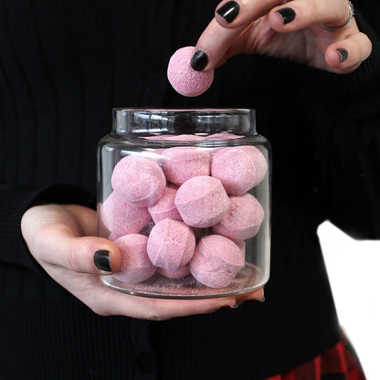 Aufbewahrungsglas aus Borosilikatglas – 25 CM: transparentes Glas mit pinken, runden Bonbons, in Händen gehalten, wobei ein Bonbon hineingelegt wird