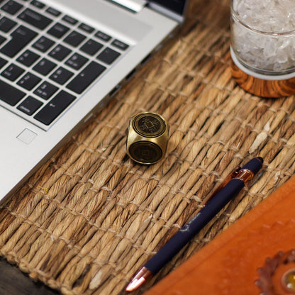 Brass Ancient Fortune Spinner – 3x3 CM Zodiac Emblems on desk mat beside laptop and pen, close-up of brass zodiac cube