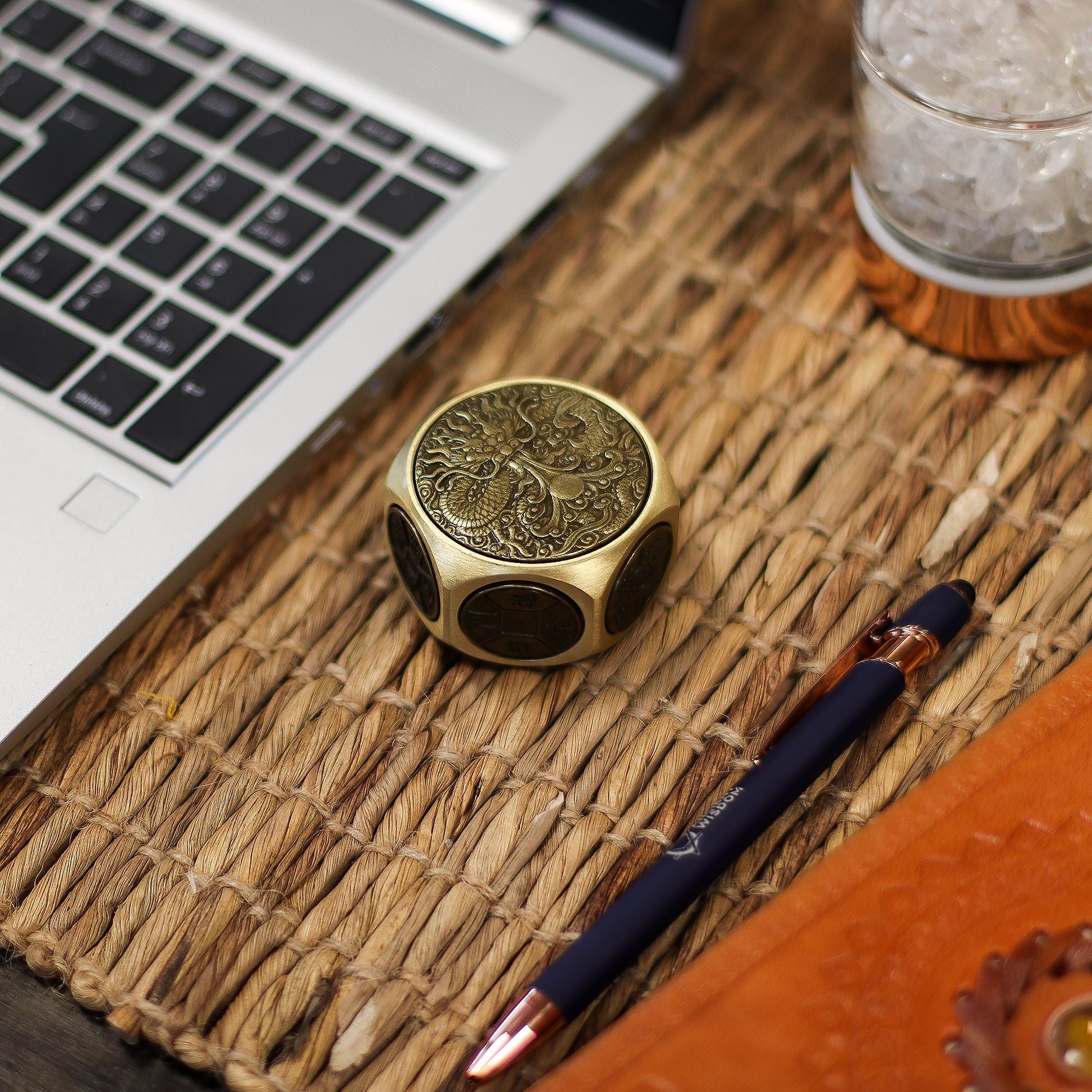 Brass Ancient Fortune Spinner – 5x3.2 CM de latón con grabado de dragón sobre escritorio junto a portátil, bolígrafo y vaso