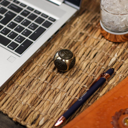 Alt Tag: Brass Ancient Fortune Spinner – Rounded 3.5 CM de latón con motivos de moneda china sobre escritorio junto a laptop y bolígrafo