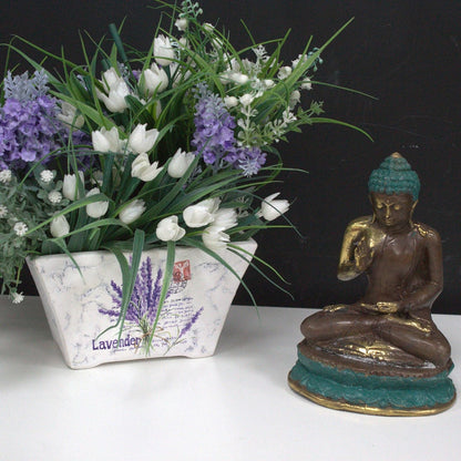 Alt Tag: Estatua de Buda de latón – Decoración Feng Shui de latón 10x5 CM en pose sentada junto a un arreglo de flores blancas y moradas