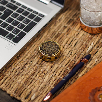 Alt Tag: Brass Feng Shui Energy Disc – 2x4.5 CM de latón sobre tapete tejido junto a laptop y bolígrafo