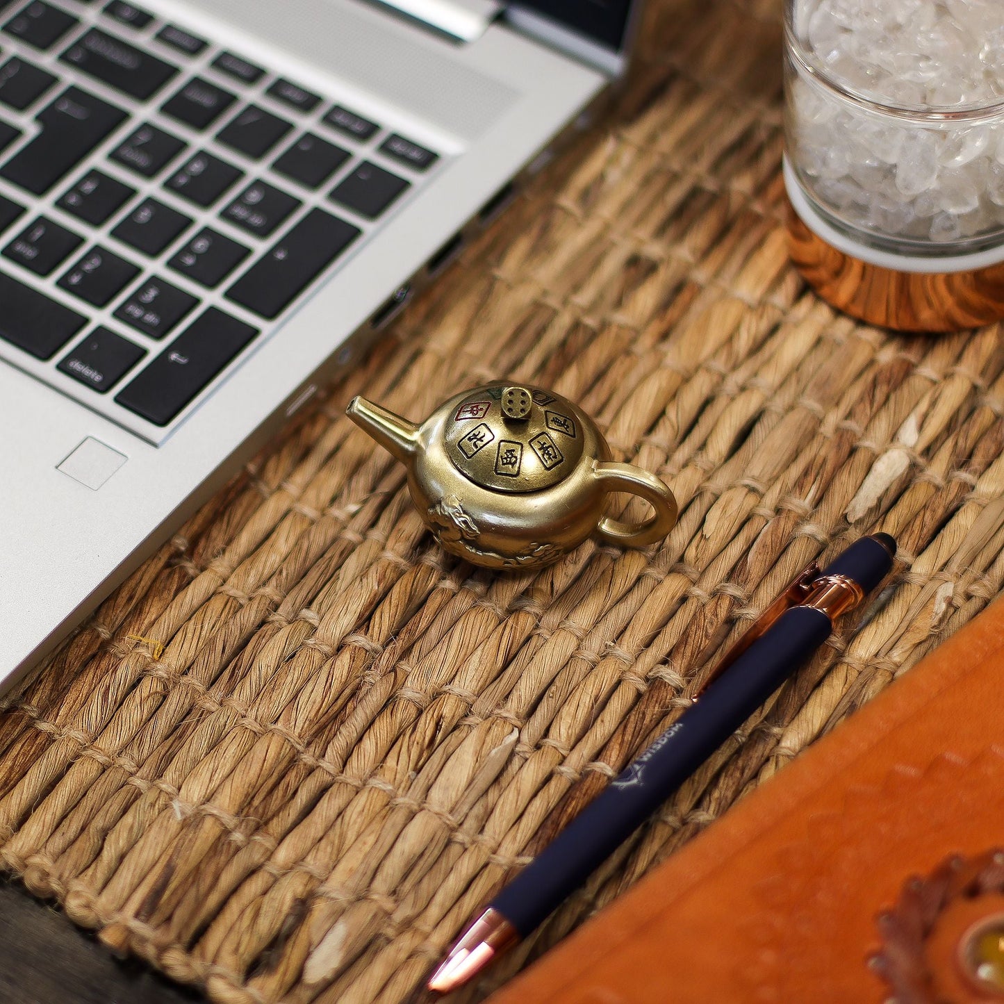 Brass Feng Shui Teapot Spinner – 8x4.5 CM de latón sobre tapete tejido junto a laptop y bolígrafo