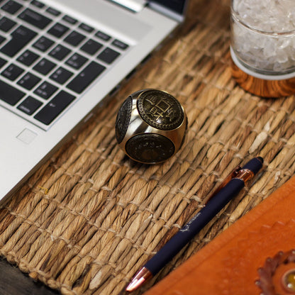 Brass Feng Shui Wealth Spinner – 5.5 CM on woven desk mat beside laptop, pen and glass, showing engraved Chinese coin design