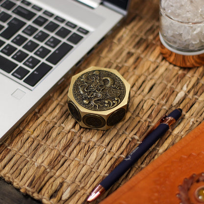Alt Tag: Brass Fortune Spinner – 6.5x3 CM de latón con grabado de dragón, sobre escritorio junto a laptop y bolígrafo