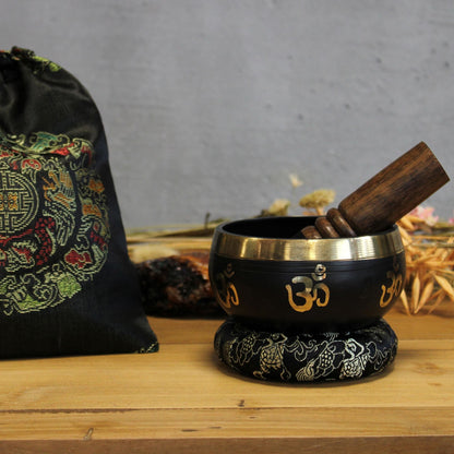 Alt-tag: Set med tibetansk sjungande skål i mässing – 9x5 cm i mässing med träklubba, broderad kudde och tygpåse på bordet