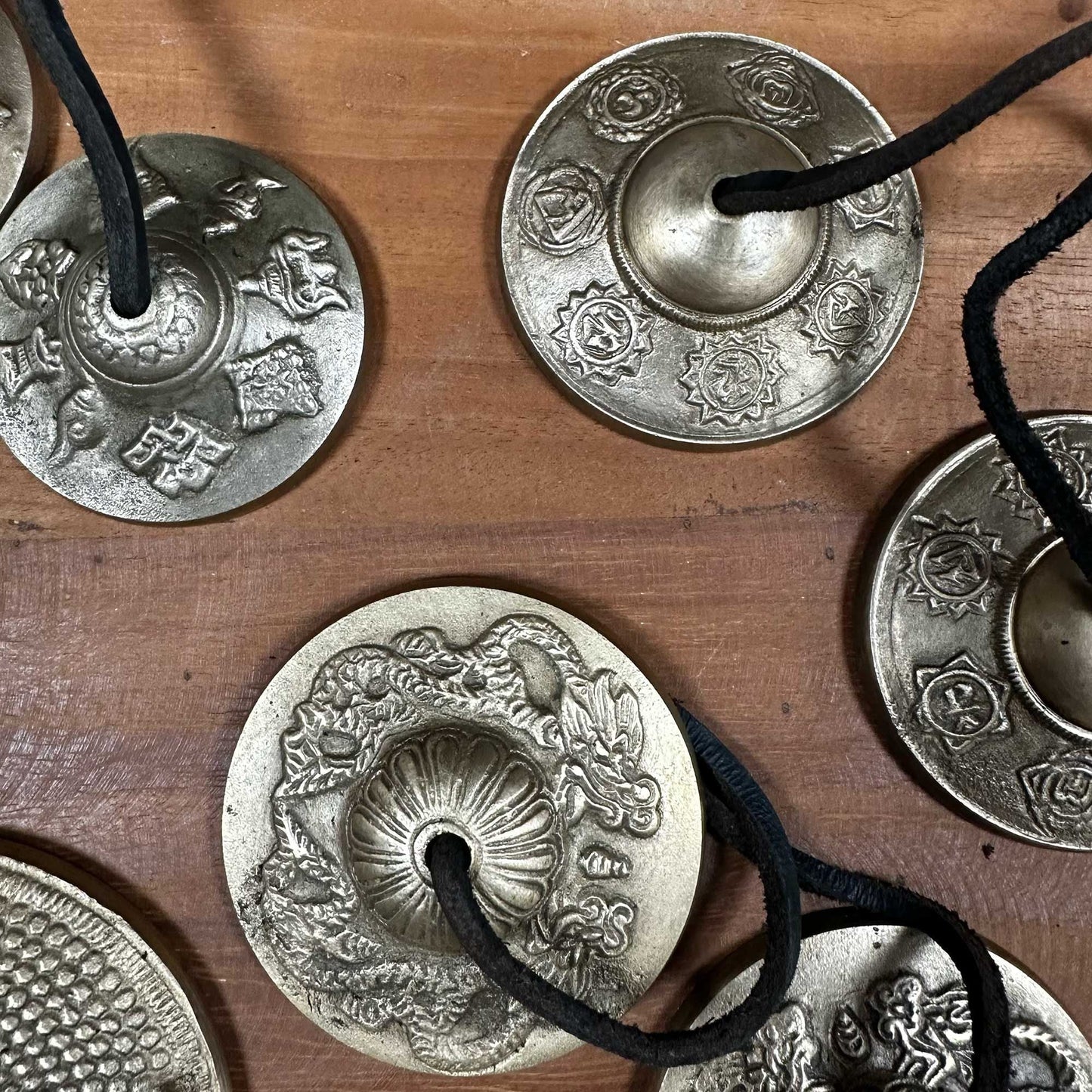 Alt Tag: Brass Tibetan Tingsha Bells – 9.5 CM de latón con diseño Five Buddha, campanas tingsha con cordón negro sobre superficie de madera