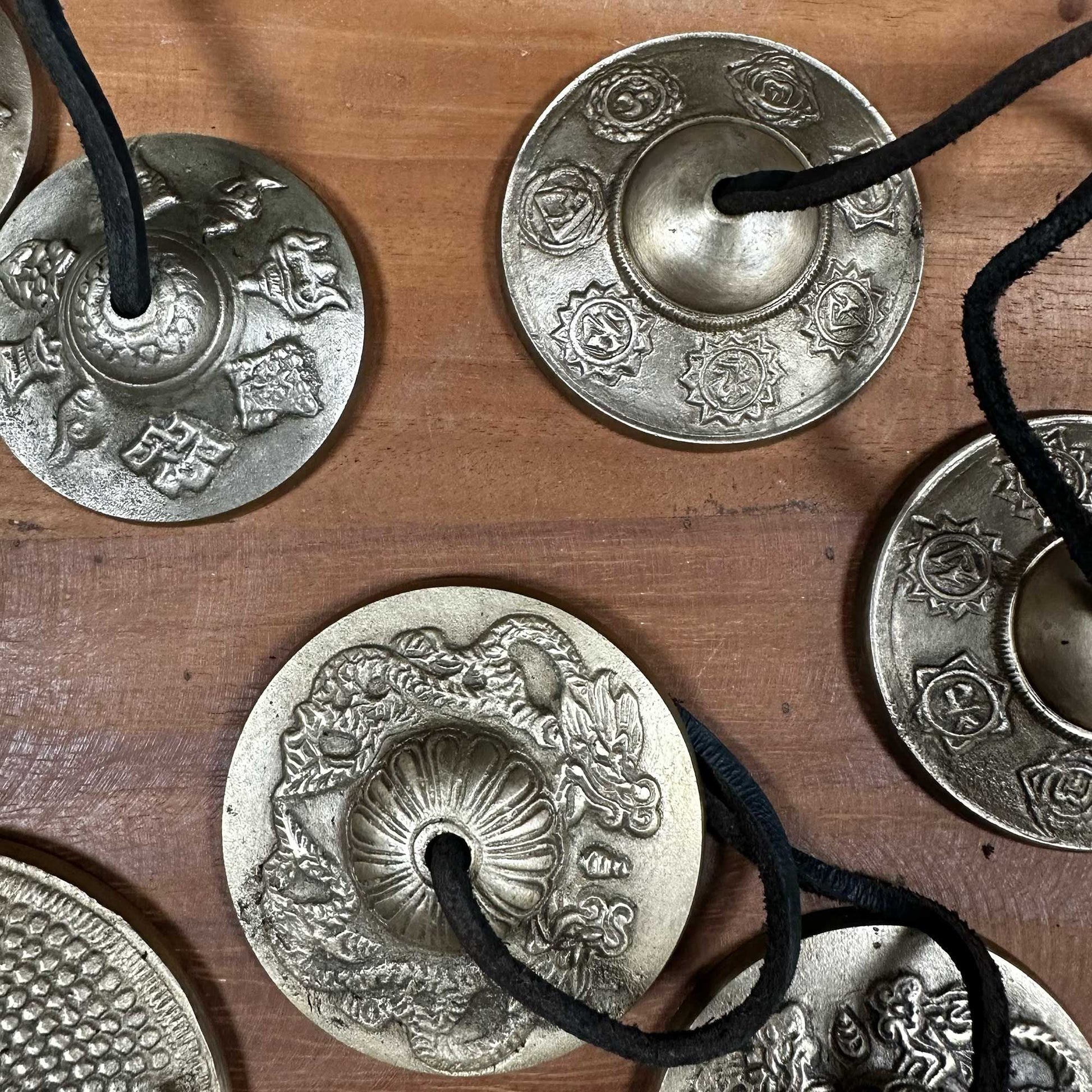 Alt Tag: Brass Tibetan Tingsha Bells – 9.5 CM de latón con diseño Five Buddha, campanas tingsha con cordón negro sobre superficie de madera