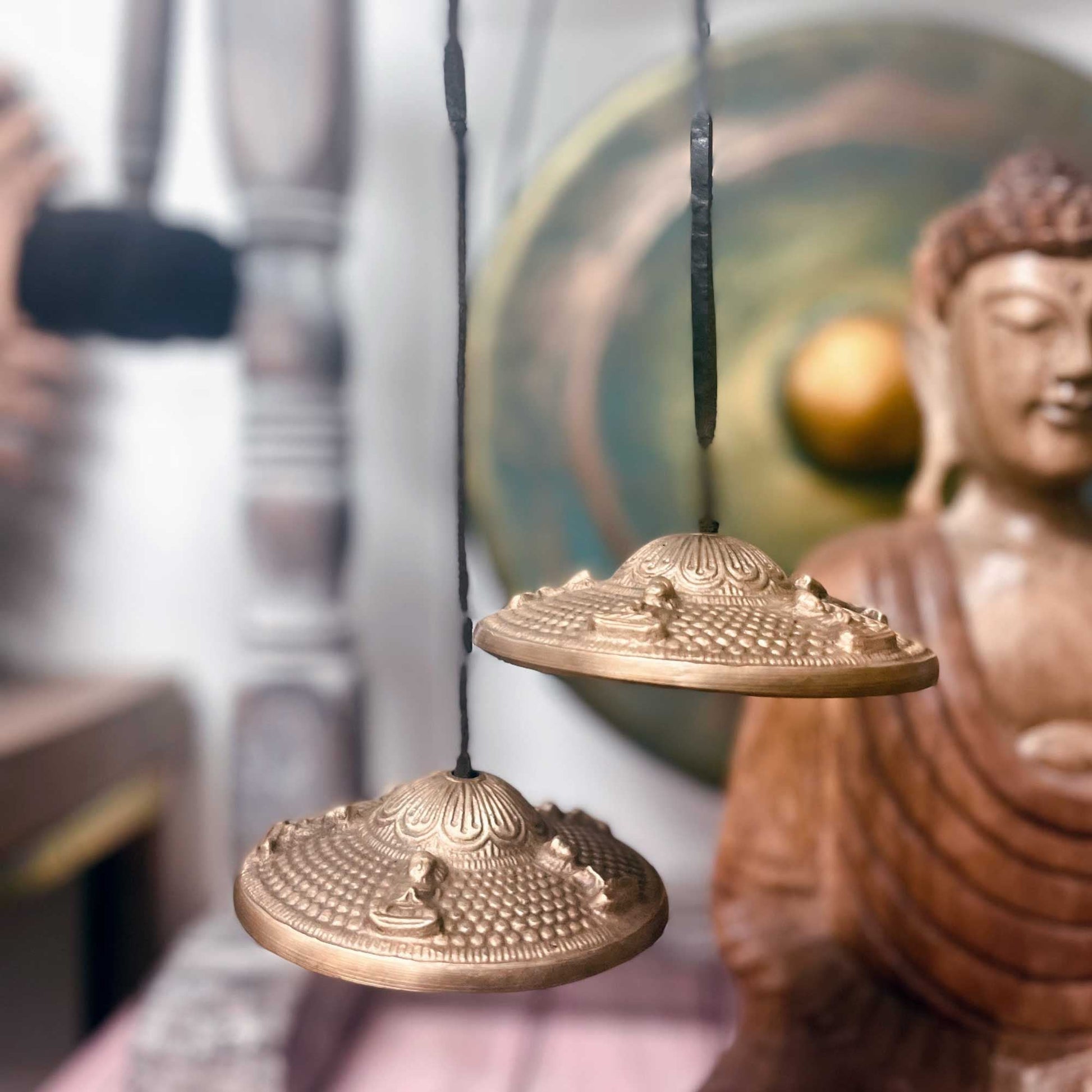 Brass Tibetan Tingsha – Dragon 7.4 CM brass tingsha cymbals with dragon design, hanging on cord with Buddha statue in background