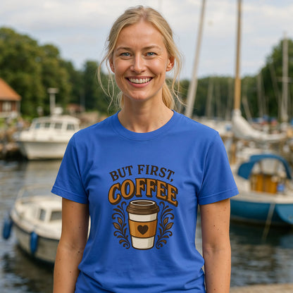 Alt Tag: But First Coffee 100% Organic Cotton T-Shirt blue graphic tee with coffee cup design, worn by smiling woman outdoors near marina