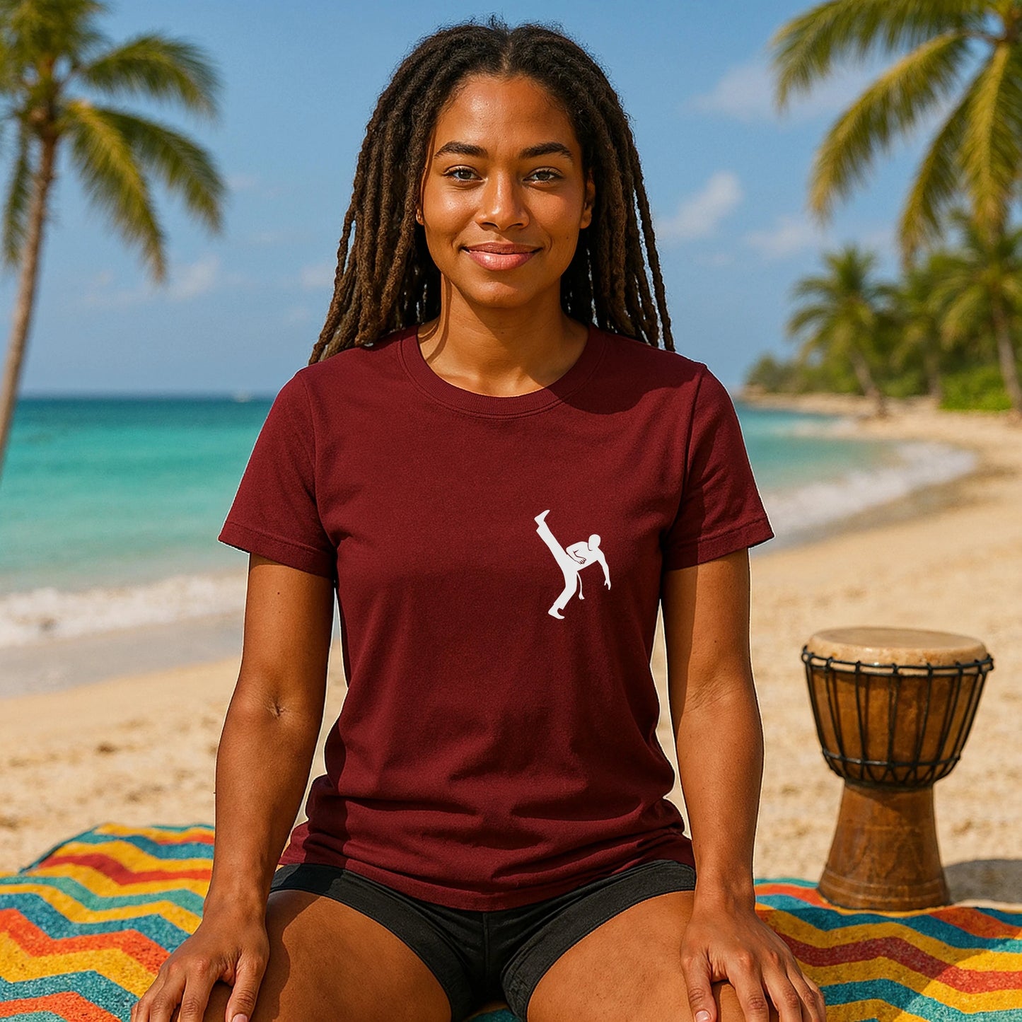 Alt Tag: Capoeira Kick 100% Organic Cotton T-Shirt burgundy tee with capoeira kick graphic, worn by woman sitting on beach