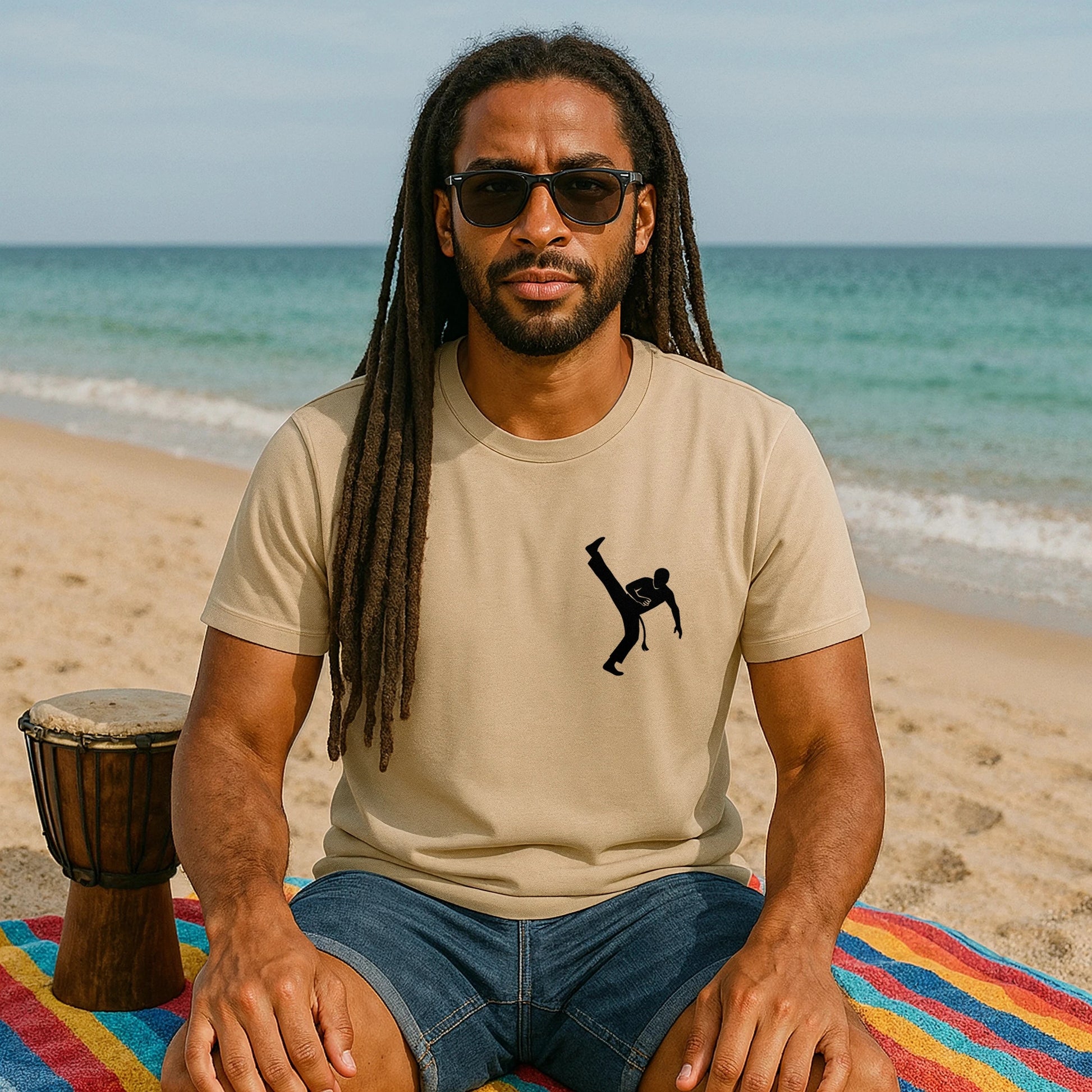 Capoeira Kick 100% Organic Cotton T-Shirt beige tee with capoeira kick graphic worn by man sitting on beach