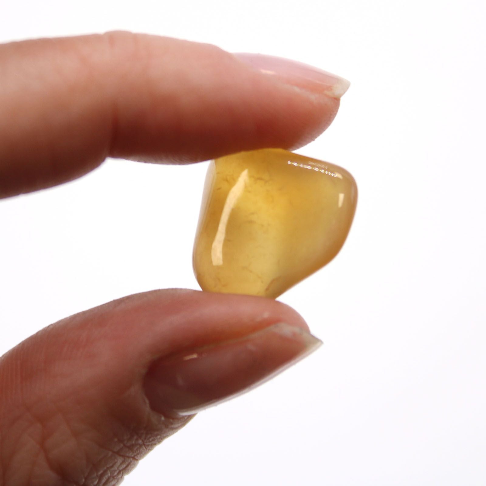 Carnelian Agate Tumble Stones – 24-Piece Set: piedra rodada de ágata cornalina sostenida entre los dedos, tono amarillo anaranjado