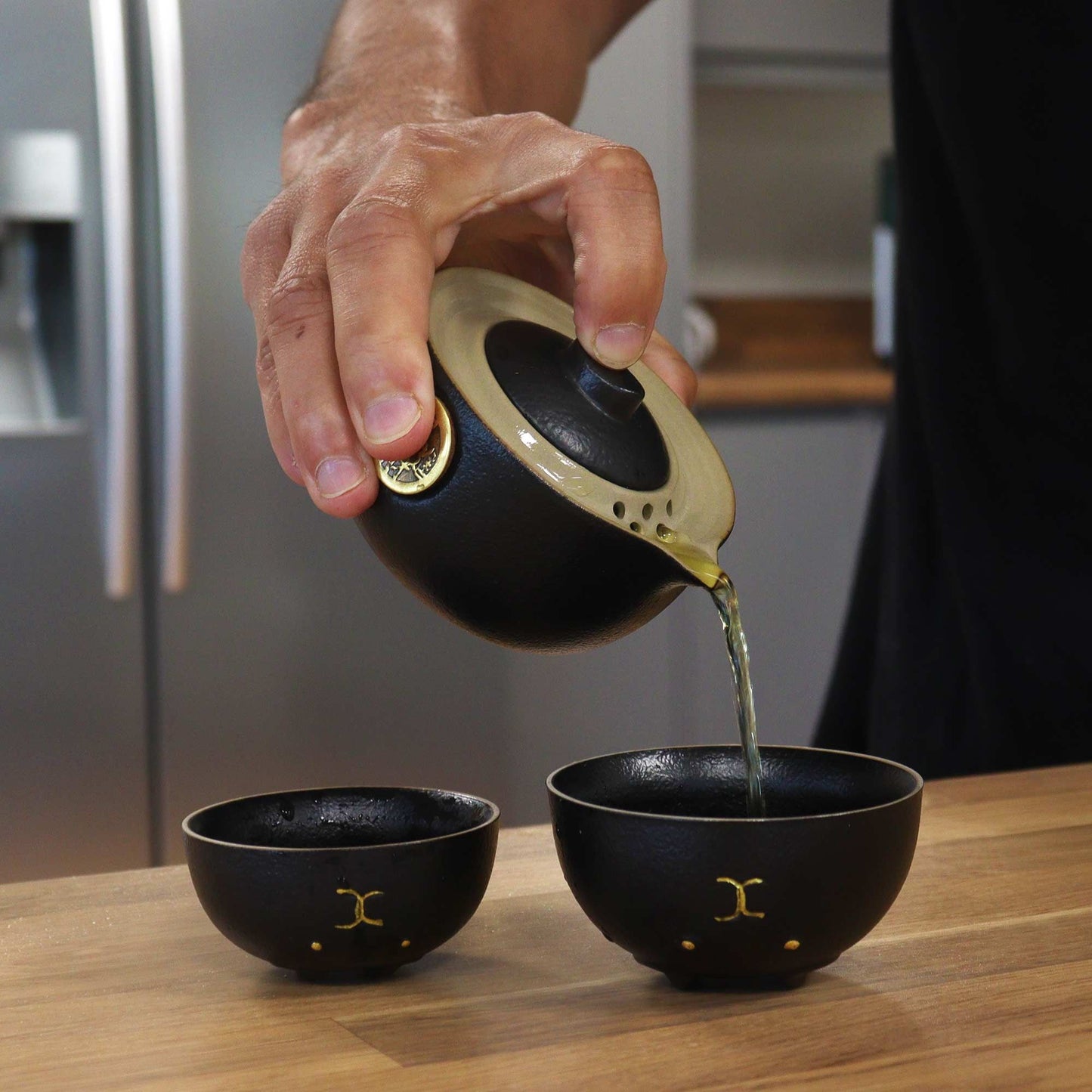 Alt Tag: Ceramic Money Cat Teapot Set – 2 Cups Black pouring tea into black ceramic cup with gold accents on wooden table