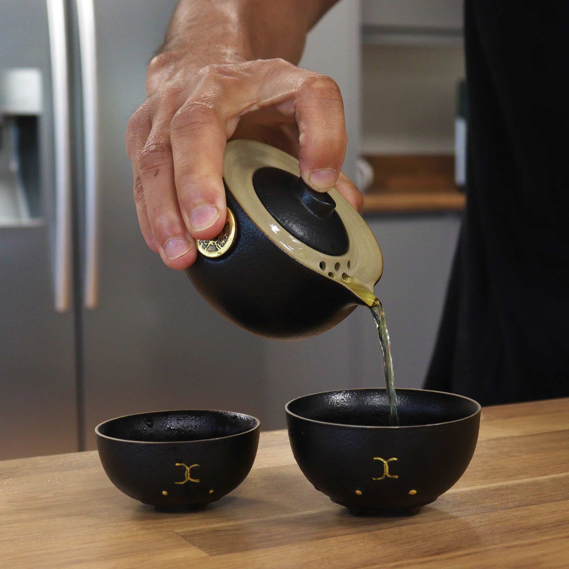 Alt Tag: Ceramic Money Cat Teapot Set – 2 Cups Black pouring tea into black ceramic cup with gold accents on wooden table