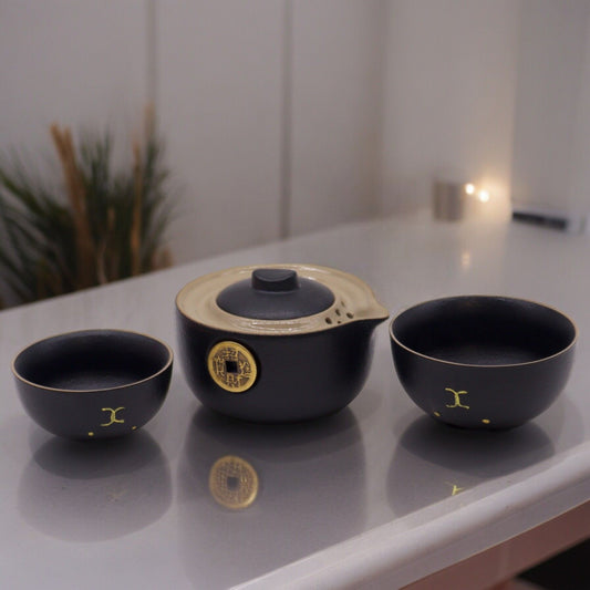 Alt-Tag: Keramik-Geldkatzen-Teekannen-Set – 2 Tassen Schwarz mit schwarzer Keramik-Teekanne und zwei Tassen, goldenes Geldmotiv auf der Tischplatte