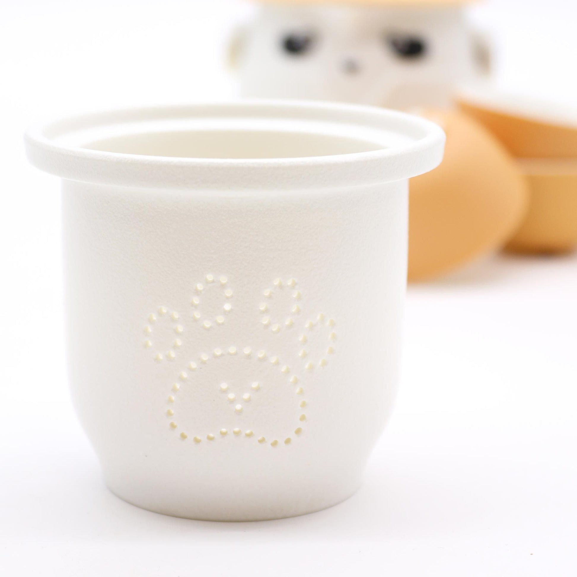 Alt Tag: Ceramic Panda Teapot Set – Orange white ceramic cup with paw print detail, orange cups blurred in background