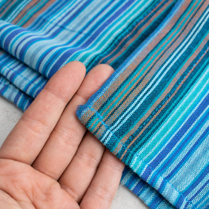 Fingers supporting a folded edge of the turquoise and blue striped shirt, with the woven texture visible.
