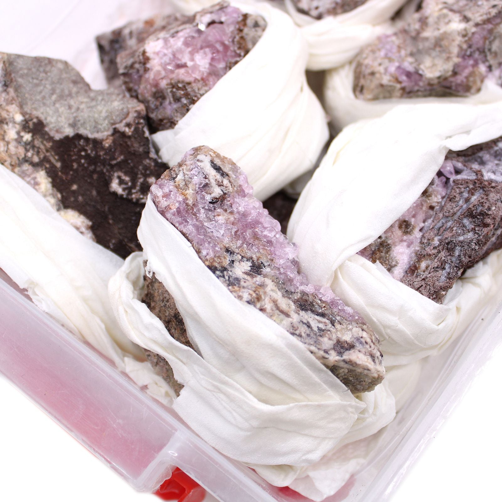 Alt Tag: Cobalt Calcite Mineral Specimens – 25 Pieces, pink-purple rough mineral rocks wrapped in tissue inside a storage container