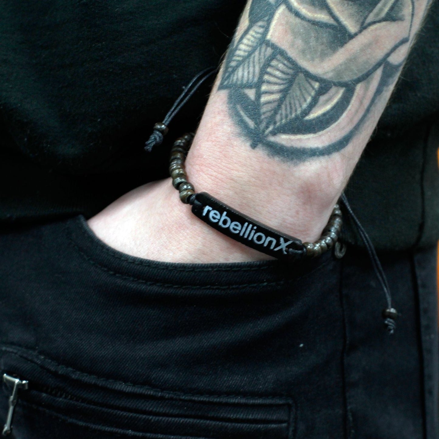 Alt-tag: Armband i kokosnötsträ med slogan – Rebellion X bangle på handleden, hållbart kokosnötsträ, svart slogan ”rebellionX”, 7.5x3x0.5 cm