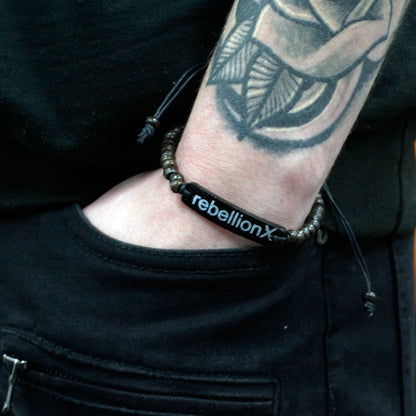 Alt-tag: Armband i kokosnötsträ med slogan – Rebellion X bangle på handleden, hållbart kokosnötsträ, svart slogan ”rebellionX”, 7.5x3x0.5 cm