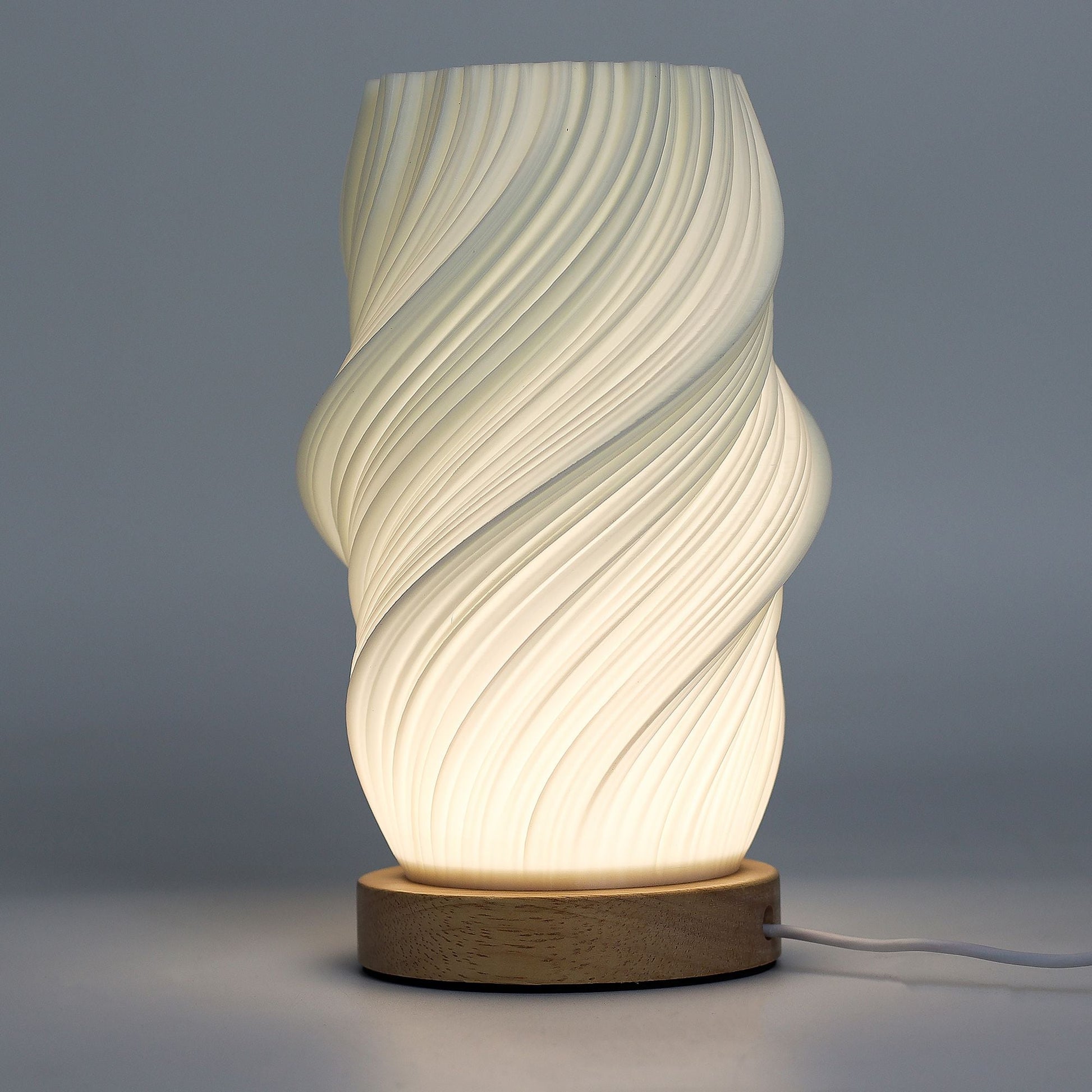 Alt Tag: Cornstarch PLA New Wave Lamp – Cloud Twisted, lámpara de mesa moderna con pantalla blanca en espiral y base de madera, encendida