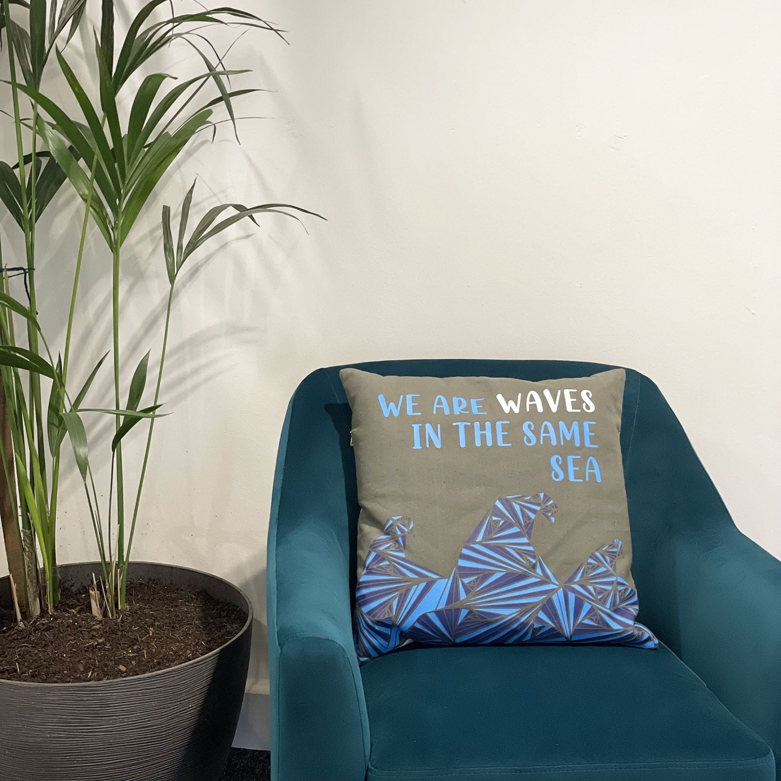 Cotton Poem Cushion Cover – We Are Waves, Natural – 45x45 CM on teal chair with “We are waves in the same sea” text