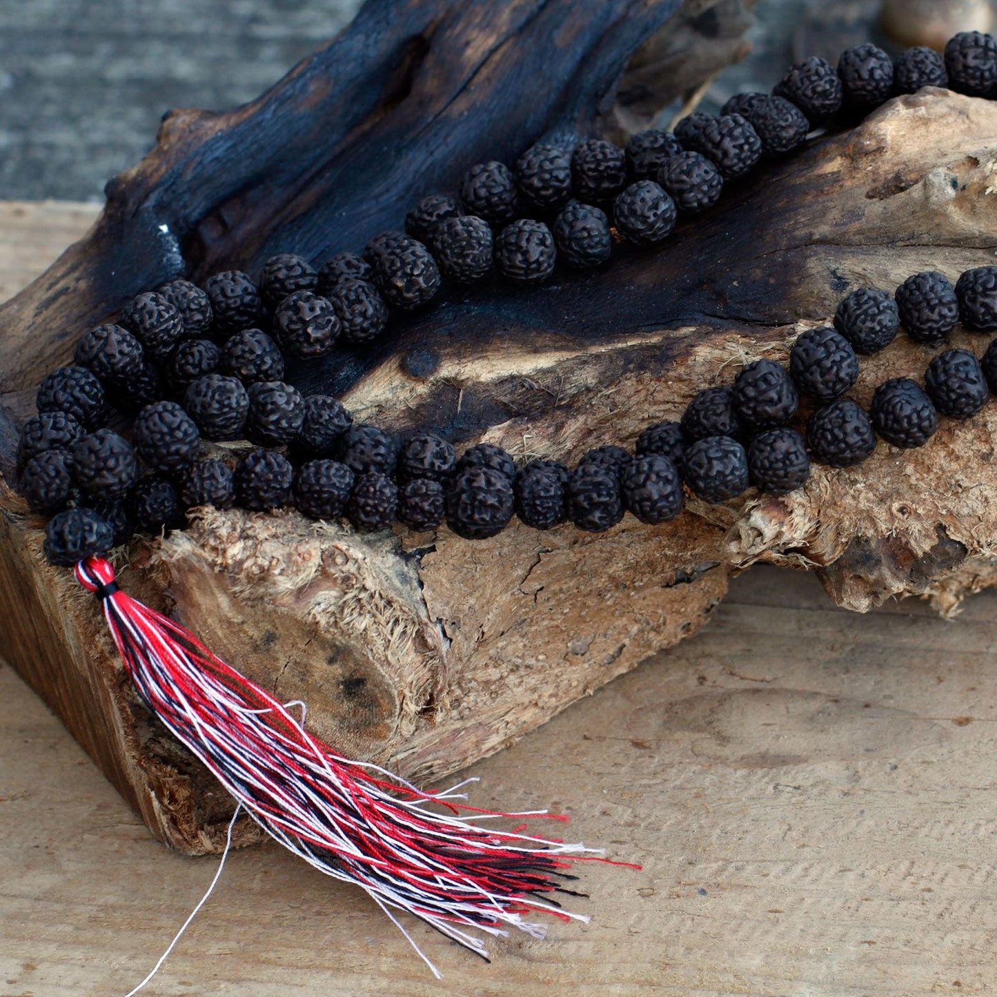 Dark Wood Beads Rudraksha Mala – 108 CM con cuentas oscuras y borla roja y blanca sobre madera rústica