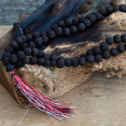 Dark Wood Beads Rudraksha Mala – 108 CM con cuentas oscuras y borla roja y blanca sobre madera rústica