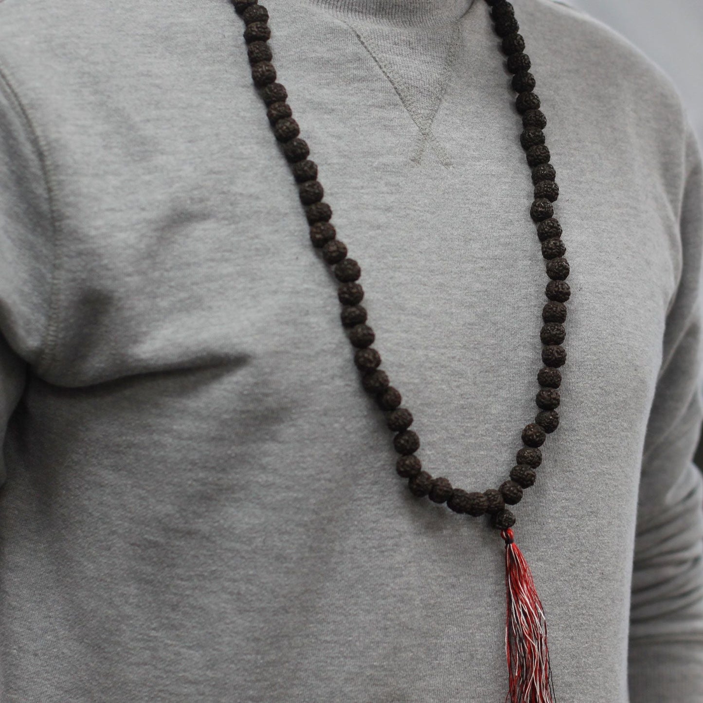 Alt Tag: Dark Wood Beads Rudraksha Mala – 108 CM con cuentas oscuras y borla roja, collar de meditación en persona con suéter gris