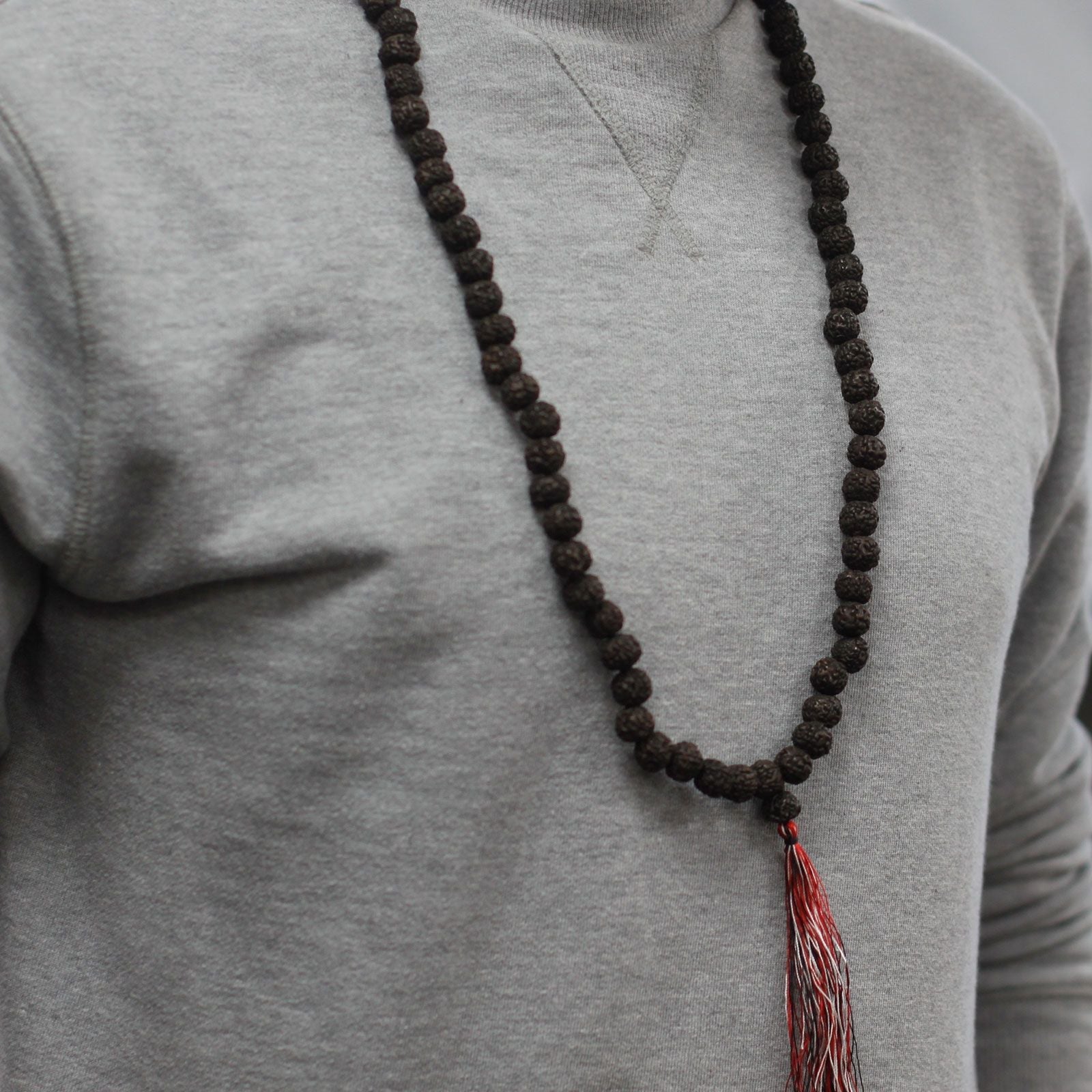 Alt Tag: Dark Wood Beads Rudraksha Mala – 108 CM con cuentas oscuras y borla roja, collar de meditación en persona con suéter gris